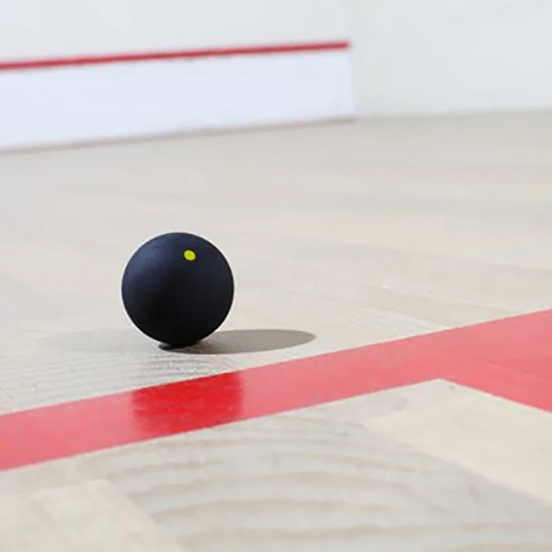 Balle de squash professionnelle en caoutchouc noir posée sur un terrain avec marqueur rouge.