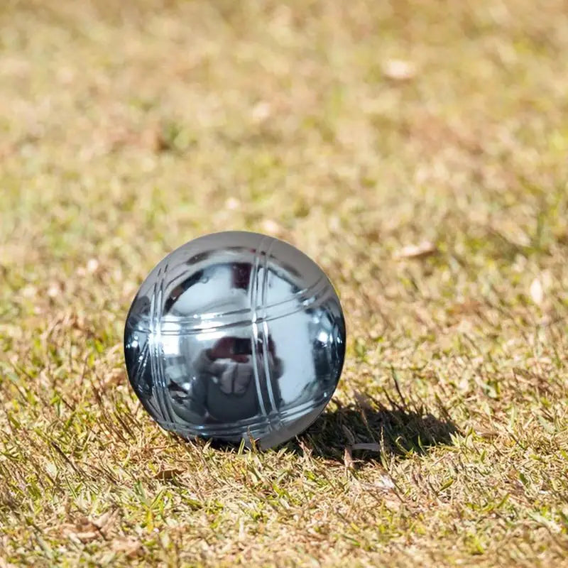 Boule de pétanque en métal gravé, posée sur l'herbe, unique et élégante, idéale pour la pétanque.